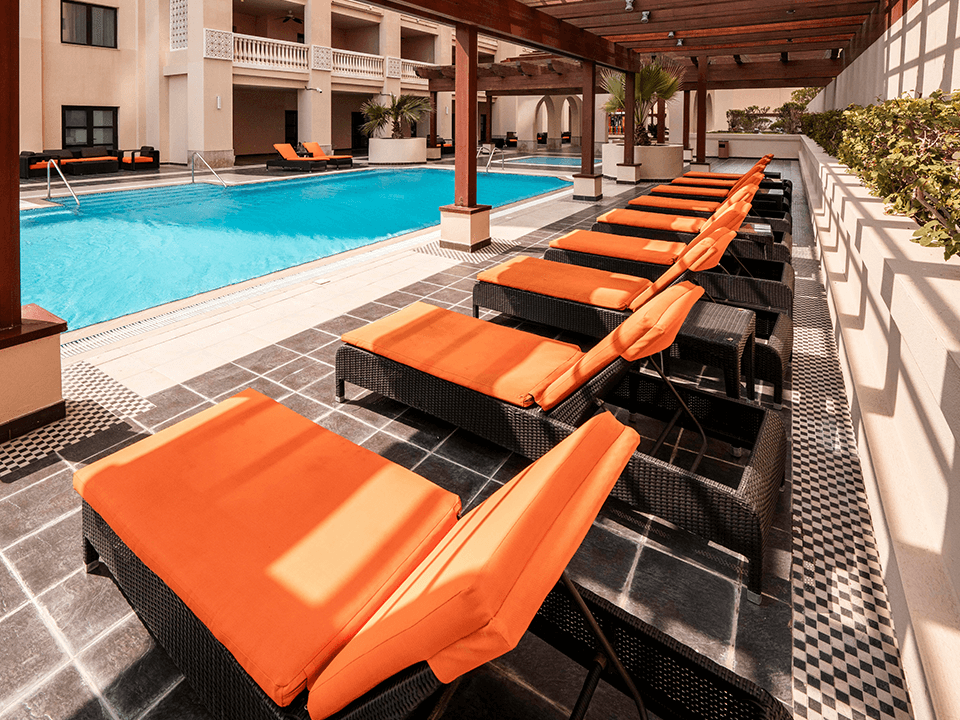 Outdoor wicker chaise lounges with striped cushions on a balcony, representing refreshed poolside cushions ready for the summer season.